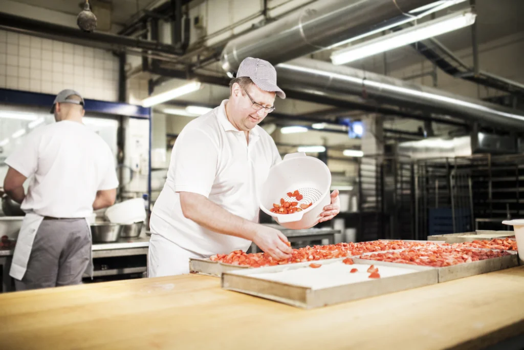 Foto: Mitarbeiter belegt in einer Bäckerei Kuchen mit Erdbeeren (© Ernährung-NRW e. V.)